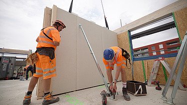 Foto von Holzbauarbeiten mit Kran und Bauarbeiter:innen