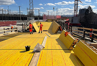 Nachtaufnahme einer STRABAG-Baustelle. Ein grosser Kran steht beleuchtet neben einem Wohnhaus unter dem klaren Nachthimmel.