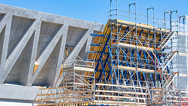 Zwei grosse Hebevorrichtungen auf einer STRABAG-Baustelle. Im Hintergrund sind Bauarbeiter:innen und ein Kran zu sehen.
