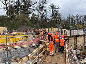 Schulklasse mit Schutzhelmen geht über einen Holzsteg auf einer Baustelle in Kloten.