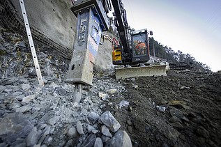 Bagger spitzt den Fels auf, im Vordergrund Geröll