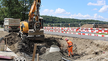 Foto von Arbeiten an einer Baugrube ein Bauarbeiter in Orange und ein Bagger