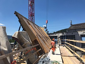  Ein Kran der STRABAG hebt nachts ein langes Brückenteil über Bahngleise. Die Baustelle ist hell erleuchtet.