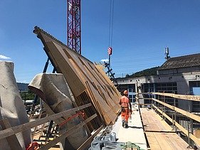  Ein Kran der STRABAG hebt nachts ein langes Brückenteil über Bahngleise. Die Baustelle ist hell erleuchtet.