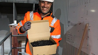 Mann mit Schachtel, in der heisser Asphalt drin ist.