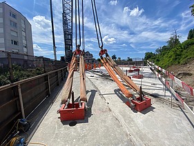 Zwei grosse Hebevorrichtungen auf einer STRABAG-Baustelle. Im Hintergrund sind Bauarbeiter:innen und ein Kran zu sehen.