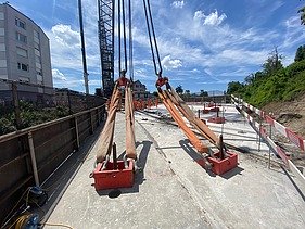 Zwei grosse Hebevorrichtungen auf einer STRABAG-Baustelle. Im Hintergrund sind Bauarbeiter:innen und ein Kran zu sehen.