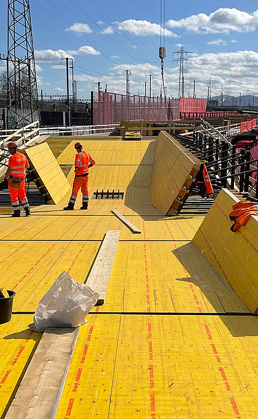 Nachtaufnahme einer STRABAG-Baustelle. Ein grosser Kran steht beleuchtet neben einem Wohnhaus unter dem klaren Nachthimmel.