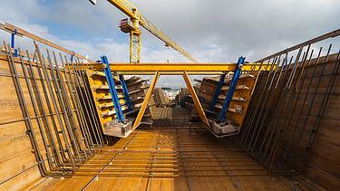 Nahaufnahme der Baustelle mit Schalungselementen und Kran im Hintergrund