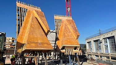  Ein Kran der STRABAG hebt nachts ein langes Brückenteil über Bahngleise. Die Baustelle ist hell erleuchtet.