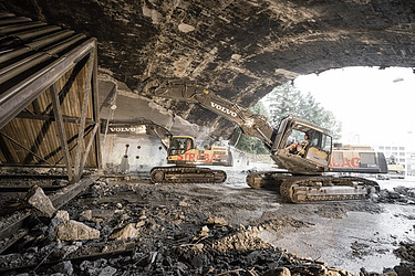 Zwei STRABAG-Bagger führen unter einer Brückenkonstruktion Abbruch- und Rückbauarbeiten im Ingenieurbau durch.