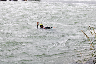 Eine Person in Schutzkleidung treibt während eines Wasserrettungskurses in einem schnell fliessenden Fluss und hebt einen Arm als Signal.
