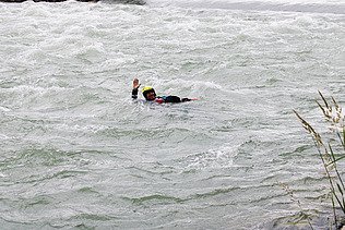 Eine Person in Schutzkleidung treibt während eines Wasserrettungskurses in einem schnell fliessenden Fluss und hebt einen Arm als Signal.
