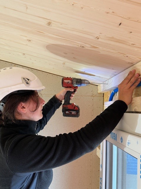 Zimmerin schraubt einen Nagel in einen Balken mit einem Akkuschrauber