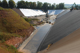 Blick auf eine weitläufige Baustelle mit steilen Böschungen, unten verläuft ein schmaler Weg entlang der Baufläche.