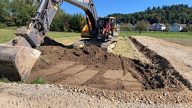 Zwei grosse Hebevorrichtungen auf einer STRABAG-Baustelle. Im Hintergrund sind Bauarbeiter:innen und ein Kran zu sehen.