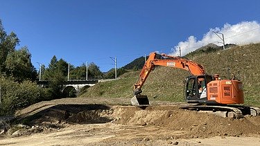 Schutz vor Naturgefahren - STRABAG Ingenieurbau Bagger der STRABAG am Aclettbach bei Disentis gräbt ein Fundament, im Hintergrund eine Eisenbahnbrücke