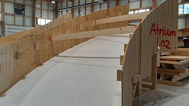  Ein Kran der STRABAG hebt nachts ein langes Brückenteil über Bahngleise. Die Baustelle ist hell erleuchtet.