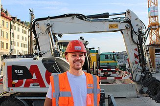 Leonard Berger mit Helm und Weste vor einer Baumaschine auf der Baustelle Rathausbrücke