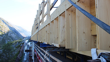 Ein Gerüst und Holzelemente einer STRABAG Baustelle in den Schweizer Bergen bei schönem Wetter.