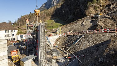 Bau einer massiven Betonmauer mit Kran, Gerüst und Maschinen zur Geländesicherung im Gebirge.