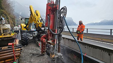 Nahaufnahme mit schwerem Gerät und Mitarbeitern, im Hintergrund der Vierwaldstättersee
