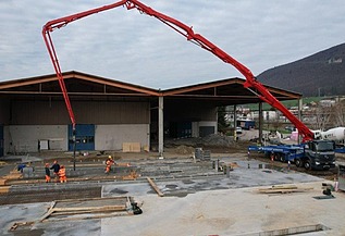 Die Baustelle «Erweiterung Bourquin» mit einem grossen, roten Betonpumpen-Lastwagen, der Beton für die Gebäudeerweiterung liefert.
