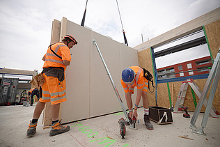 Foto von Holzbauarbeiten mit Kran und Bauarbeiter:innen