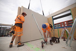 Foto von Holzbauarbeiten mit Kran und Bauarbeiter:innen