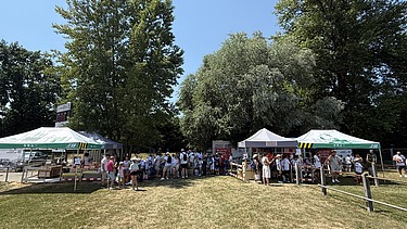 STRABAG Stand in voller Breite mit Maurer-, Pflaster-, Nivellier- und Simulator-Posten. Viert Zelte und viele Menschen sind zu sehen.