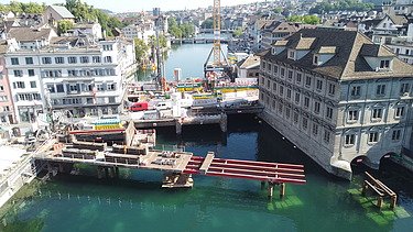 Bild zeigt die Baustelle mit Kran in der Bildmitte, mit der Hilfsbrücke zur Hälfte fertig gebaut