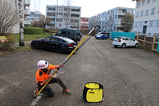 STRABAG Sicherheitsbeauftragter mit Wurfschleuder und Führungsseil auf einem Parkplatz. Im Hintergrund stehen einige Autos.