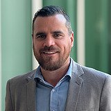 Technischer Bereichsleiter im Anzug lächelt in die Kamera. Im Hintergrund ist ein Lift zu sehen.