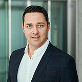 Kaufmännischer Bereichsleiter im Anzug lächelt in die Kamera. Im Hintergrund ist ein Lift zu sehen.