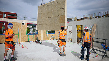 Foto von Holzbauarbeiten mit Kran und Bauarbeiter:innen