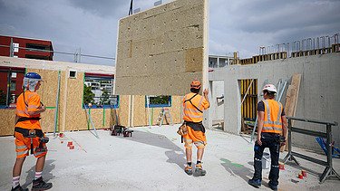 Foto von Holzbauarbeiten mit Kran und Bauarbeiter:innen