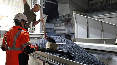 Zwei Männer entnehmen eine Asphaltprobe aus dem geladenen Lastwagen