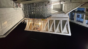  Ein Kran der STRABAG hebt an einem sonnigen Tag ein grosses Brückenelement. Im Hintergrund stehen mehrere Personen auf der Baustelle, neben einem Wohngebäude.
