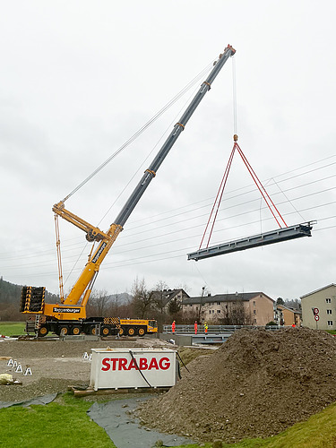 Kran mit Stahlseilen und Brückenelement hinter STRABAG Contrainer