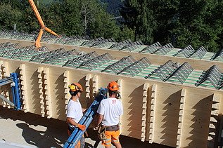 Zwei Arbeiter in Schutzkleidung richten einen frisch eingehobenen Holzträger millimetergenau aus