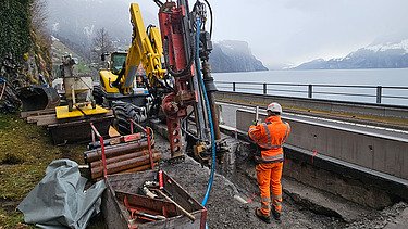 Nahaufnahme mit schwerem Gerät und Mitarbeitern, im Hintergrund der Vierwaldstättersee