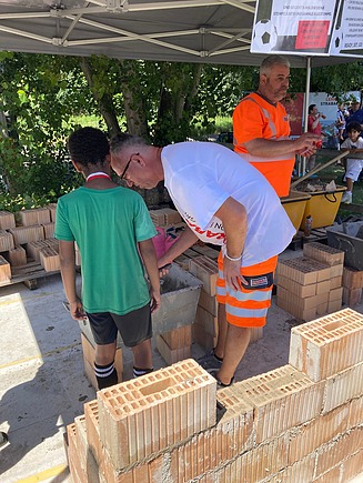 STRABAG-Zelt: Kinder und Erwachsene bauen unter Anleitung eine Mauer aus Ziegeln.