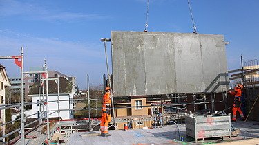 Foto von zwei Baustellenarbeiter die eine Wand einsetzen mit Hilfe eines Krans