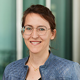 Kommunikation's Leiterin lächelt in die Kamera. Im Hintergrund ist ein Lift zu sehen.