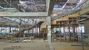  Ein Kran der STRABAG hebt nachts ein langes Brückenteil über Bahngleise. Die Baustelle ist hell erleuchtet.