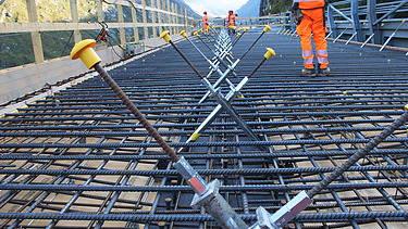 Bauarbeiter:innen stehen auf einer Bewehrung aus Stahlmatten, um Beton für eine neue Brücke in den Bergen zu giessen.