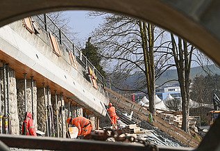 Mehrere STRABAG-Arbeiter in orangefarbener Schutzkleidung sind im Hintergrund an einer Betonwand tätig.