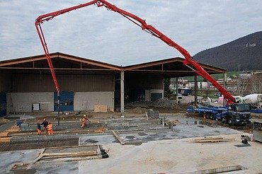Erweiterung Bourquin - STRABAG Hochbau Die Baustelle «Erweiterung Bourquin» mit einem grossen, roten Betonpumpen-Lastwagen, der Beton für die Gebäudeerweiterung liefert.