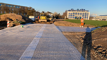  Ein Kran der STRABAG hebt nachts ein langes Brückenteil über Bahngleise. Die Baustelle ist hell erleuchtet.