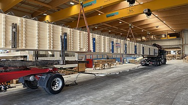 Verladen eines Holzträgers auf einen Lastwagen in einer Halle.